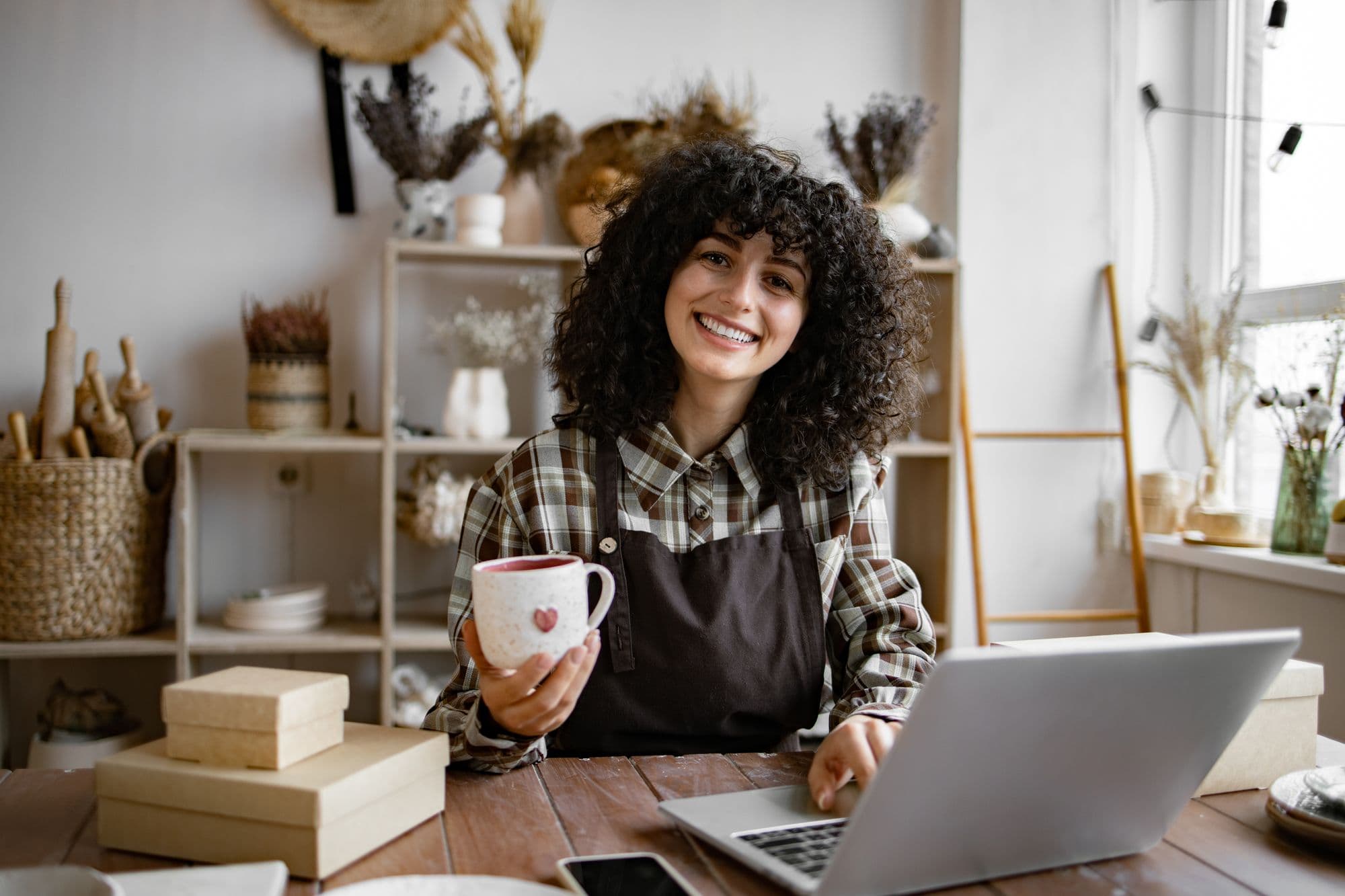 Small business owner smiling while working on a laptop in her shop